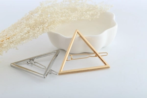 Detail of minimalist geometric triangle hair clips in polished gold and silver metal