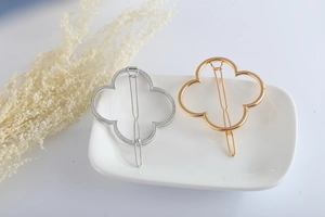 Detail showing gold and silver clover metal hair clips on a white ceramic plate