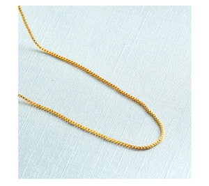 Close-up of a gold-plated box chain necklace with metallic luster on blue background