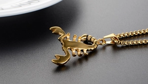 Close-up of golden scorpion pendant necklace with detailed box chain on a grey surface