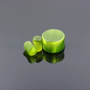 Macro shot of three green cat eye stone ear plugs with silky luster on reflective surface