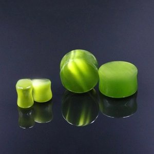 Detailed view of polished green cat eye stone ear plugs with natural chatoyancy effect