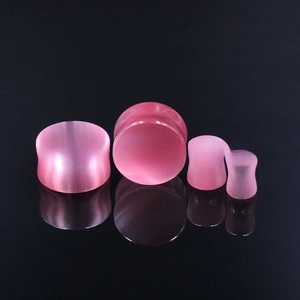 Macro detail of pink cat-eye stone ear plugs in four sizes on a black surface