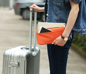 Hand holding an orange felt travel organizer bag with smartphone against a suitcase
