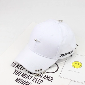 Detail of white cotton baseball cap with metal rings on brim and safety pin decoration
