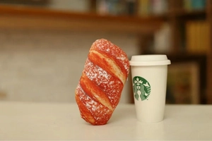 Close-up of a plush baguette pillow next to a coffee cup showing soft texture and size