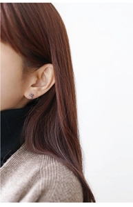 Close-up of S925 sterling silver cross earring on model wearing beige cardigan