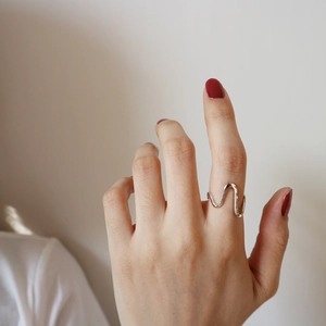Detail of minimalist wavy S925 sterling silver ring worn on a finger with elegant red nails