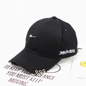 Detail of black baseball cap with metal rings on brim and safety pin with ball