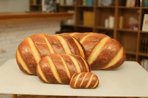 Detailed comparison of realistic bread plush pillows in four different sizes on a white stand