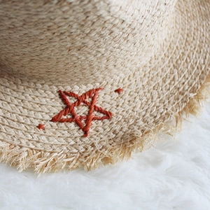 Macro detail of natural straw hat texture with red embroidered star and fringed edge