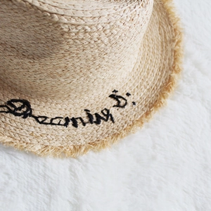 Macro detail of the Dreaming embroidery and raffia texture on a frayed edge straw hat
