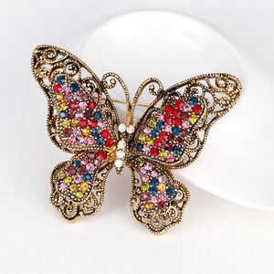 Vintage bronze butterfly brooch with colorful crystals on a white ceramic plate