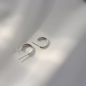 Close-up of minimalist S925 sterling silver C-shape stud earrings on white silk fabric