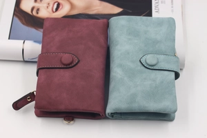 Detail of burgundy and light blue matte PU leather wallets with round buckles on a magazine