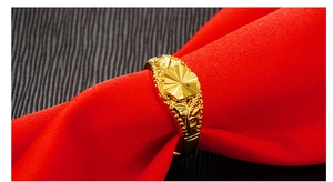 Close-up of golden ring featuring intricate flower patterns on a red fabric background