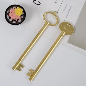 Golden key-shaped creative pens with KRD-315 engraving and metallic finish on white surface