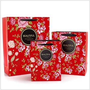 Three sizes of red floral gift bags with gold lettering and sturdy handles