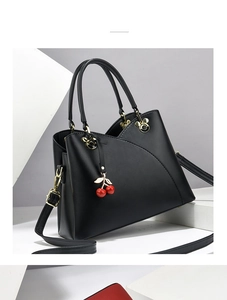 Detail of black faux leather handbag with golden Mickey-shaped hardware and cherry charm