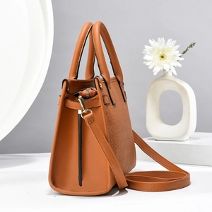 Detail view of brown leather handbag featuring embossed crocodile texture and gold hardware
