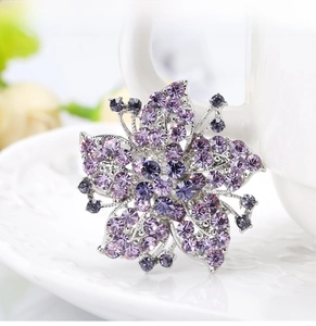Detailed close-up of a silver flower brooch with purple crystals on white ceramic