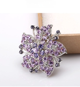Detail of flower brooch featuring purple crystals and silver alloy base on white backdrop
