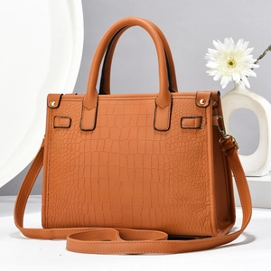 Detail of crocodile embossed leather texture and gold hardware on brown handbag