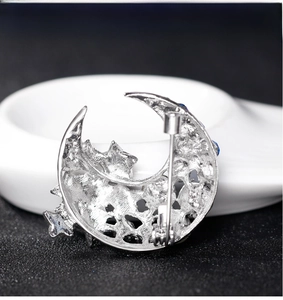 Macro detail of silver crescent moon brooch back with star cutouts and blue stones