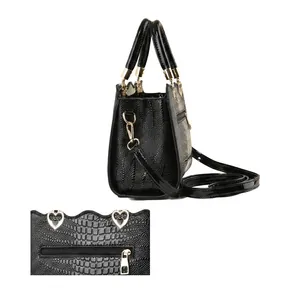 Détail d'un sac à main noir brillant motif crocodile avec un cœur doré et zip latéral