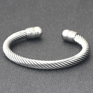 Detail of silver twisted cable cuff bracelet with round ends on a textured gray background