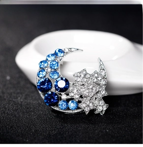 Macro shot of silver moon and star brooch with blue rhinestones on black background