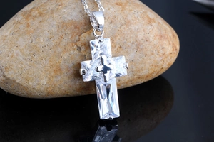 Detailed macro view of silver cross pendant with AAA cubic zirconia on natural stone