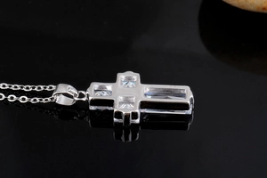 Macro side view of silver cross pendant with AAA square zircons on reflective black surface