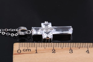Macro shot of silver cross pendant featuring AAA zircons next to a measuring ruler