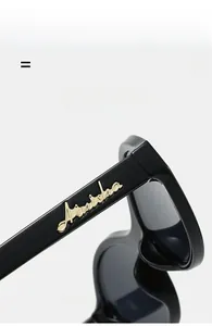 Detail of glossy black vintage cat-eye sunglasses with gold Ainisha logo on temple
