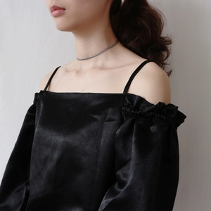 Detail of elegant black satin off-shoulder top with thin straps and delicate pleats