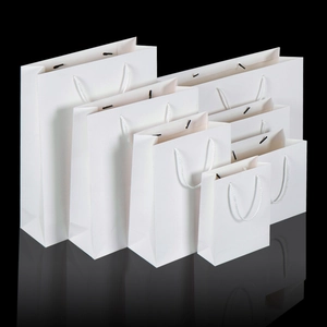 White paper gift bags in various sizes with rope handles on reflective black surface