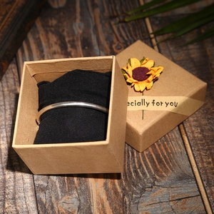 Brown kraft paper jewelry gift box with a silver bangle and black velvet pouch on wood