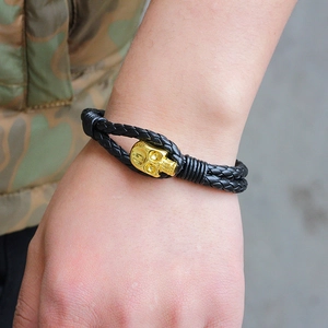 Men's braided black leather bracelet with a detailed golden skull charm on a wrist
