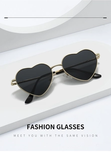 Detail view of heart-shaped gold metal sunglasses with dark lenses on a white platform