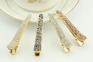 Set of four gold metal hair clips with rhinestones and white pearls on white ceramic
