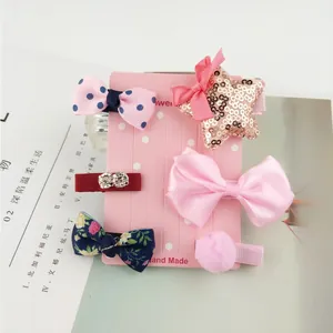 Detail showing five assorted cute hair clips for girls featuring bows and plush balls
