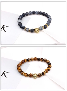 Detail of beaded tiger eye bracelets with golden leopard head charms on white background