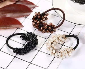 Three-piece set of handmade pearl hair ties in brown, black, and white on a grid background