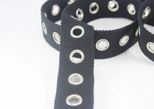Macro shot of black canvas belt featuring double-row silver metal grommets and texture