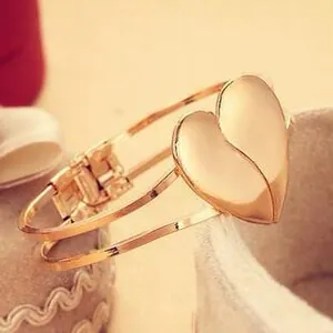 Detail of a golden double-layered heart bangle featuring a polished metallic heart centerpiece