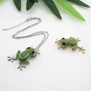 Détails du collier et de la broche grenouille avec cristaux verts sur tissu blanc