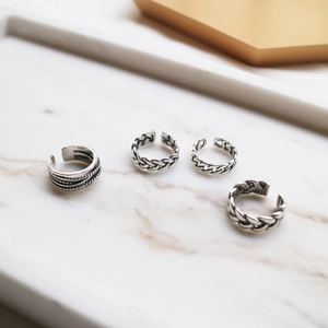 Close-up of S925 sterling silver rings with braided textures on white marble tray