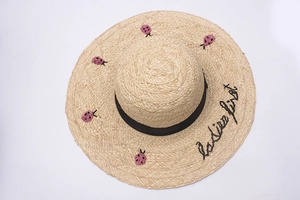 Detail of raffia straw hat with ladies first embroidery and pink ladybug patterns