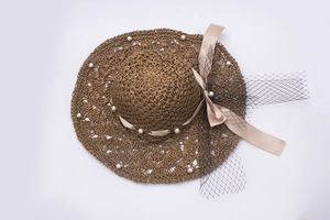 Détail d'un chapeau de soleil en paille avec bord perlé, nœud en soie et voilette